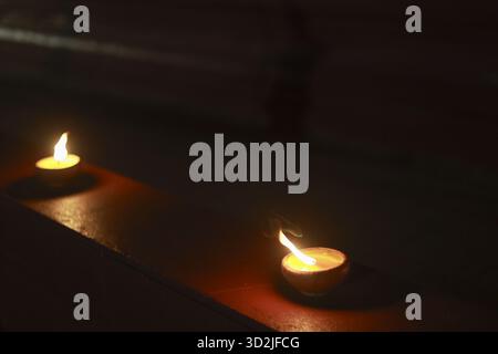 Two romantic tealight candles burning with warm flame in dark. soft light creates peaceful, spiritual glow on surface, perfect for tranquil atmosphere Stock Photo
