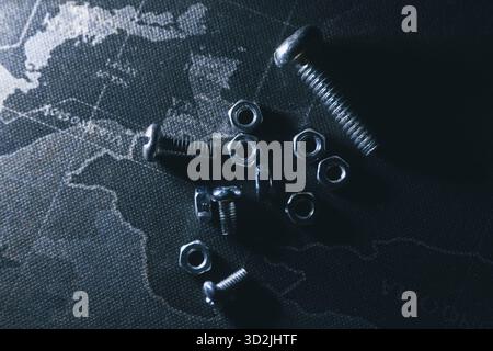 Dark abstract concept image of metal nuts and bolts scattered on global world map. monochrome and mysterious top view showing hardware, industry, and Stock Photo