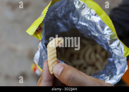 Hungry person holding delicious single crisp snack from foil bag. Eating crunchy yellow junk food treat, satisfying and savory experience. Close up vi Stock Photo
