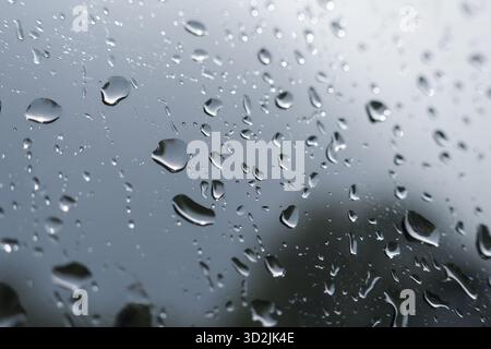 Gloomy close up of many raindrops on glass window. Abstract background with water drops creating somber texture on surface. Wet weather on grey, rainy Stock Photo