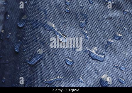 Clean close up of blue waterproof fabric with fresh water droplets beading on textured surface. protective textile background showing water resistance Stock Photo