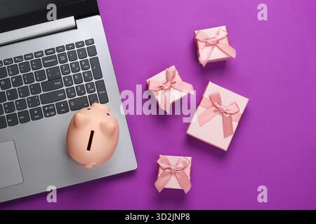 Laptop with Piggy bank and gift boxes on purple background. Minimalistic studio shot. Overhead view. Flat lay. Stock Photo