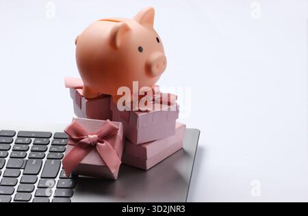 Piggy bank with stack of gift boxes on laptop keyboard closeup Stock Photo