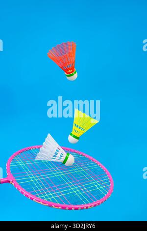 Three Colorful shuttlecocks and racket levitating isolated on blue background, for playing badminton Stock Photo