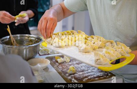 Hands of people making wontons on the kitchen table. Stock Photo
