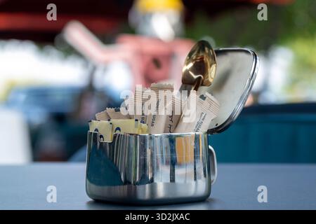 Doha, Qatar - March 10, 2025: Sugar Packets in a Big Cup with tea spoon over a coffee shop Stock Photo