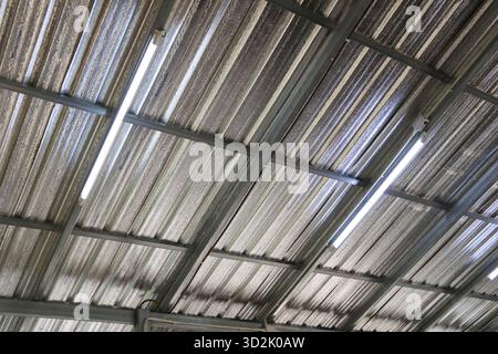 Low angle view of stark industrial ceiling with corrugated metal roof. bright light from fluorescent lamps creates repetitive pattern and texture in w Stock Photo