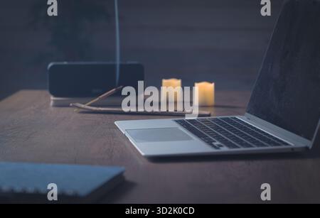 Mindful working. Serene home office table — desktop computer, aroma stick smoke, soft lamp light and gentle sound flow create creative focus Stock Photo