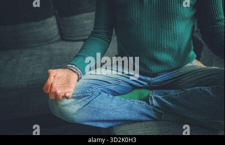 Serene young man sitting in lotus position in a cozy living room, practicing meditation and inner stillness in a tranquil atmosphere Stock Photo