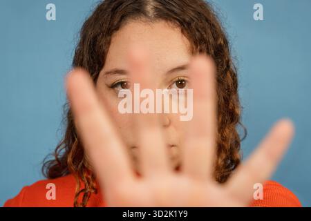 Young woman hiding her face with an open hand, showing shyness or a stop gesture Stock Photo