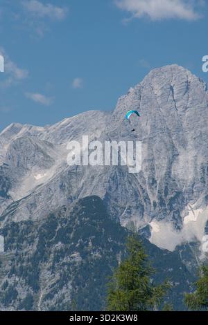 Paraglider flying over high mountain peaks in Austrian Alps under blue sky. Stock Photo