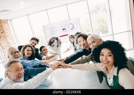Diverse team of professionals collaborating and showing teamwork enthusiastically around a table in a bright modern office Stock Photo