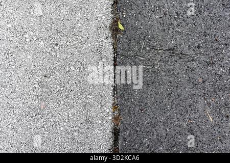 Minimalist abstract texture of asphalt road surface showing dark and light halves separated by a vertical crack with small details of grass and gravel Stock Photo