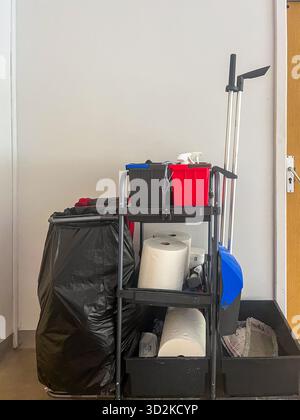 Cleaning cart displays various equipment like a broom, trash bag, and cleaning supplies, arranged neatly against a wall, emphasizing organization and Stock Photo