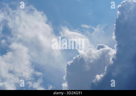 Soft, fluffy clouds float in a clear blue sky, creating a peaceful atmosphere on a warm sunny day. Stock Photo