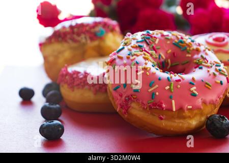 Colorful ring donuts with pink, white, and chocolate glaze, topped with sprinkles, close-up view on red background. Stock Photo