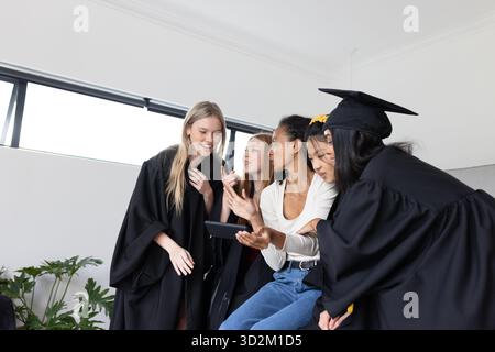 Graduating students in caps and gowns sharing joyful moments on smartphone. Graduation, celebration, academic, achievement, technology, communication || Model released Stock Photo