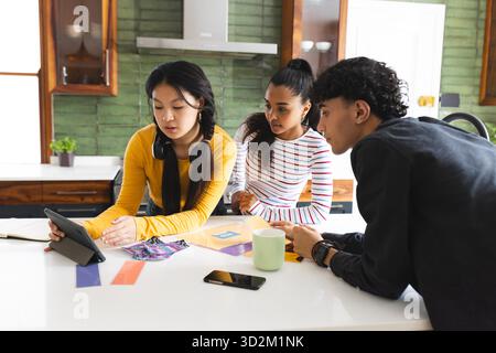 Teenagers collaborating on project using tablet in modern kitchen setting. Collaboration, teamwork, technology, brainstorming, creativity, discovery || Model released Stock Photo