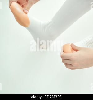 Young caucasian female dancer adjusting pointe shoes for ballet performance on white background. Stock Photo