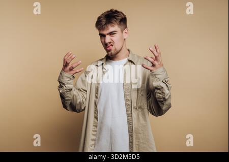 Young man expressing frustration with hands raised against beige background. Stock Photo