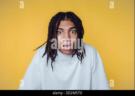 Surprised young man with braided hair against yellow background. Stock Photo