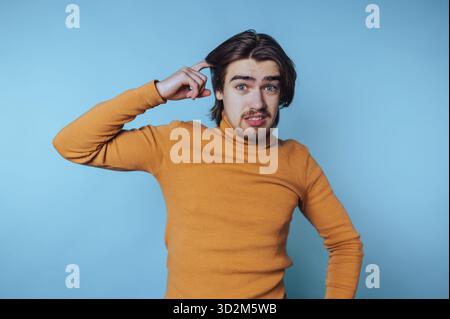 Young man in orange sweater looking confused against blue background. Stock Photo