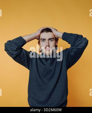 A surprised man with hands on head against an orange background. Stock Photo