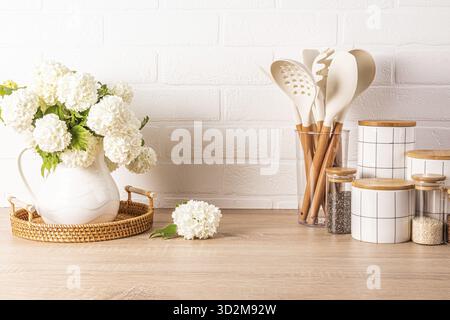 A set of tools for cooking food in a stand, a set of white ceramic jars, a jug with flowering branches in a wooden countertop. Eco style Stock Photo