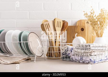 Various ceramic plates in the dryer, a set of wooden tools, kitchen towels in a mesh box, a vase with ears of wheat. Stylish kitchen background Stock Photo