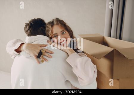 Happy young family couple man and woman hugging and holding key from new home. Moving with cardboard boxes to new estate apartment Stock Photo