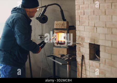 Blacksmith forge oven with hot flame. Smith put in and heating iron piece of steel in fire of red hot forge oven Stock Photo