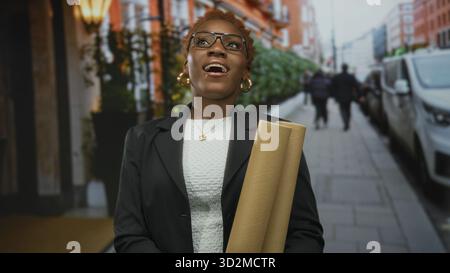 Young african american woman studying rolled blueprints while looking upward on street; confidence determination. Stock Photo