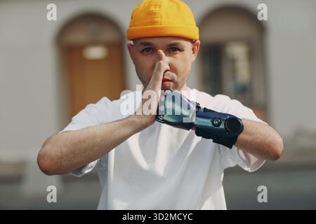 Young disabled man with artificial prosthetic hand doing yoga asana in casual clothes at outdoor city street Stock Photo