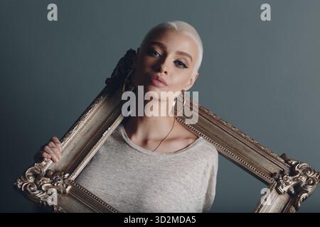 Baguette Framing Workshop Concept. Girl with short blonde hair hold gilded picture frame in hands Stock Photo