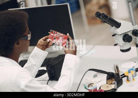 Scientist african woman working in laboratory with electronic tech instruments and microscope checking electronic plate board. Research and developmen Stock Photo