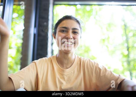 Headshot of indian woman sit on potdoor cafe waving hand looks to camera make video call chat use computer laptop webcam view, vlogger record webinar Stock Photo