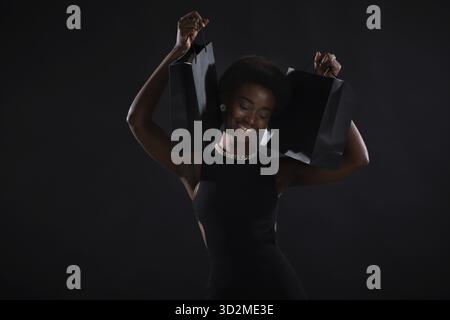 African american happy woman with afro hairstyle holds black shopping bags. Black Friday concept Stock Photo