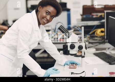Scientist african american smiling woman working in laboratory with electronic tech instruments and microscope. Research and development of electronic Stock Photo