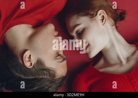 Two young people enjoying on the floor. Couple lovers man and woman laying down on red background Stock Photo