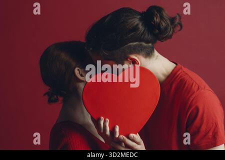 Man and woman young couple kissing and hiding behind heart-shaped box Stock Photo