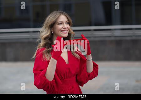 Young woman in red dress and gloves puts on medical face mask Stock Photo