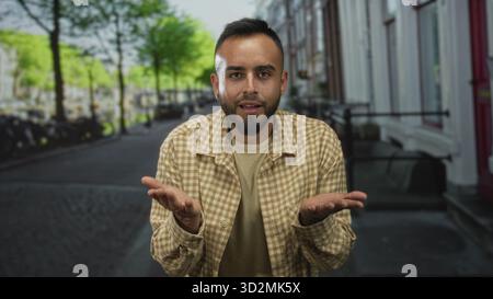 Man points finger to camera on street showing tattooed hand and beige checked shirt; community connection confidence. Stock Photo