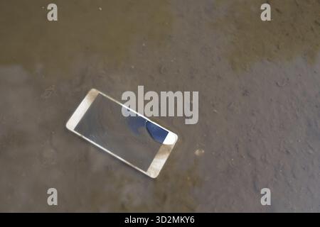 Mobile phone lying on pavement in puddle Stock Photo