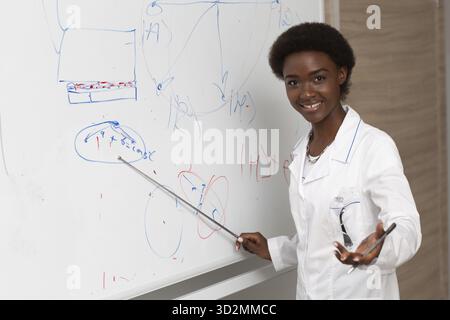 African American smiling woman math teacher stands at blackboard with pointer and smile Stock Photo