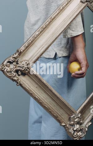 Millenial young man holds apple on hand palm in gilded picture frame Stock Photo