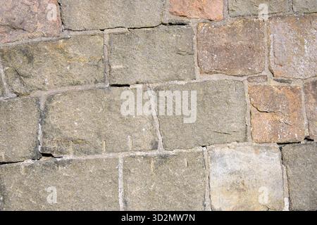 This scene features a close-up view of an ancient stone wall displaying diverse stone shapes and earthy colors. The sunlight highlights the textures a Stock Photo