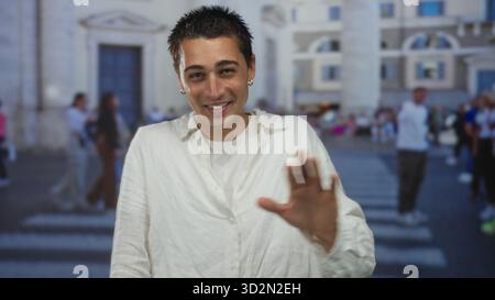 Young hispanic man smiling on urban street with people walking in background showcasing lively city life in an exterior setting with architectural ele Stock Photo