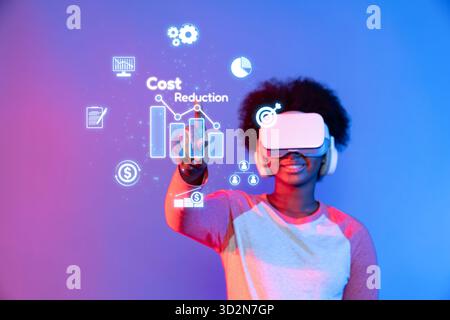 A young individual wearing virtual reality gear interacts with graphical representations of cost reduction and budget management, showcasing innovativ Stock Photo