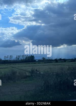 Sunbeams pierce storm clouds over Gilan’s rice paddies and distant Alborz foothills—a serene Caspian countryside moment. Stock Photo