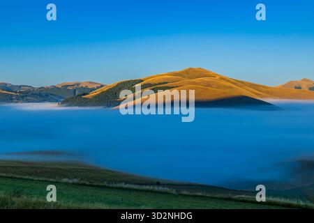 Mountains peaks emerging from a dense fog layer under clear blue sky at sunrise Stock Photo